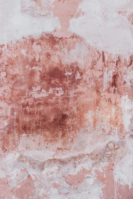 A weathered wall with peeling pink paint and exposed plaster in Wrocław, Poland