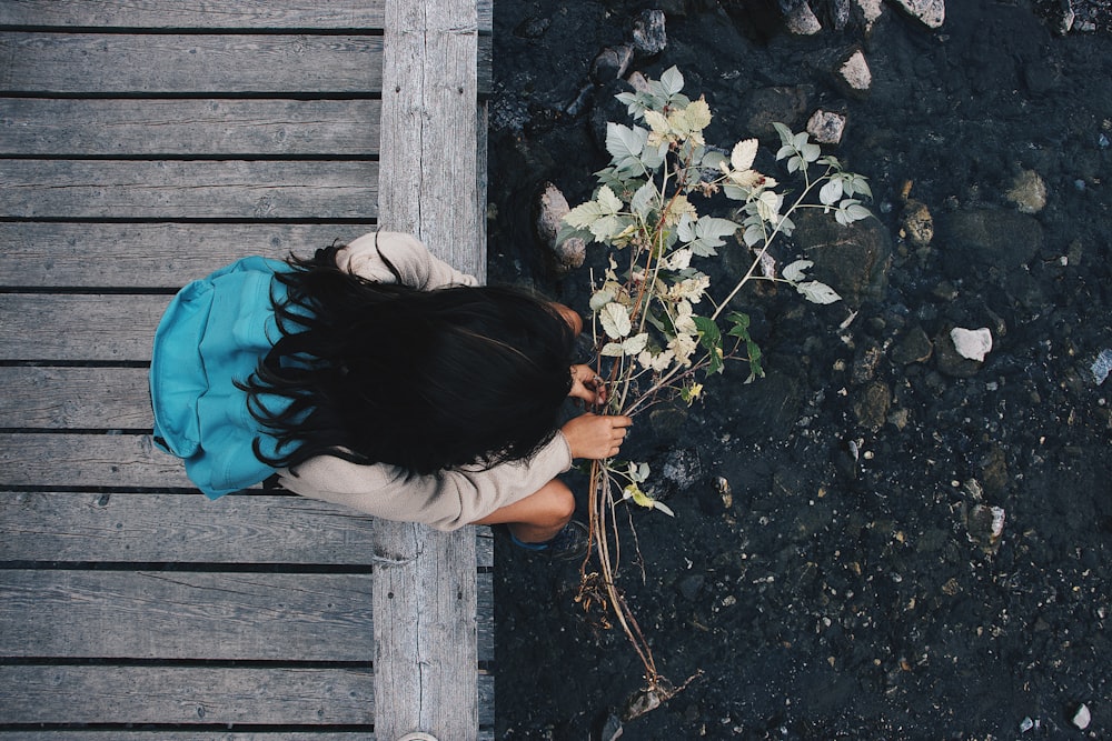 person sitting on brown wooden footbridge while holding flowers