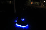 A pair of sneakers with LED soles illuminating a cosmic trail on a black surface.