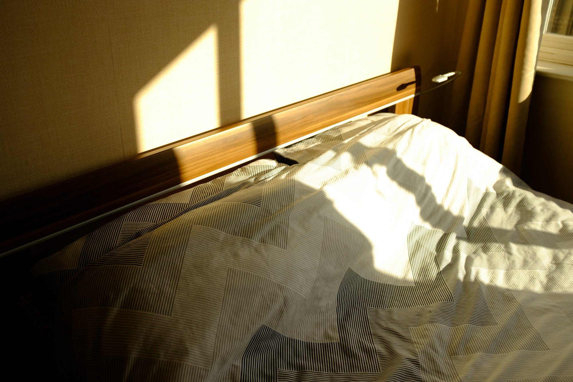 An empty, sunlit made bed in a quiet bedroom