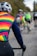 A group of cyclists riding on a road, with the focus on a rider wearing a rainbow-colored jersey and a white helmet. Other riders in various colored jerseys are in the background, slightly out of focus.