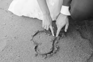 grayscale photography of man and woman draw heart on sand