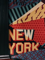 A wall mural featuring the words 'NEW YORK' in bold, colorful letters. The background consists of various geometric patterns including stripes, dots, and wavy lines in shades of blue, red, yellow, and orange.