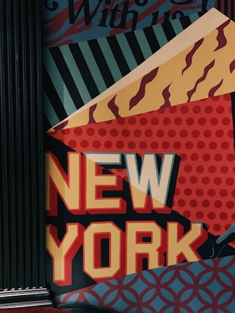 A wall mural featuring the words 'NEW YORK' in bold, colorful letters. The background consists of various geometric patterns including stripes, dots, and wavy lines in shades of blue, red, yellow, and orange.
