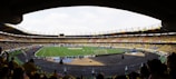 A large football stadium filled with spectators, with a green field in the center where a match is taking place. The crowd is mostly wearing yellow shirts, with some people wearing other colors. The stadium has large stands with seats, and numerous advertising banners are visible. The atmosphere appears lively and energetic.