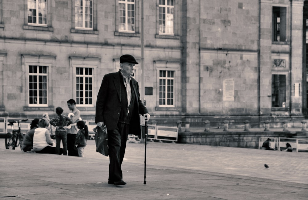 grayscale photography of man holding cane