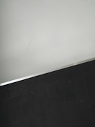 A simple interior corner with a white wall and a dark floor separated by a thin metallic strip. The wall has light scratches visible upon close inspection.