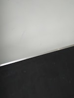 A simple interior corner with a white wall and a dark floor separated by a thin metallic strip. The wall has light scratches visible upon close inspection.