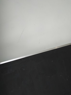 A simple interior corner with a white wall and a dark floor separated by a thin metallic strip. The wall has light scratches visible upon close inspection.