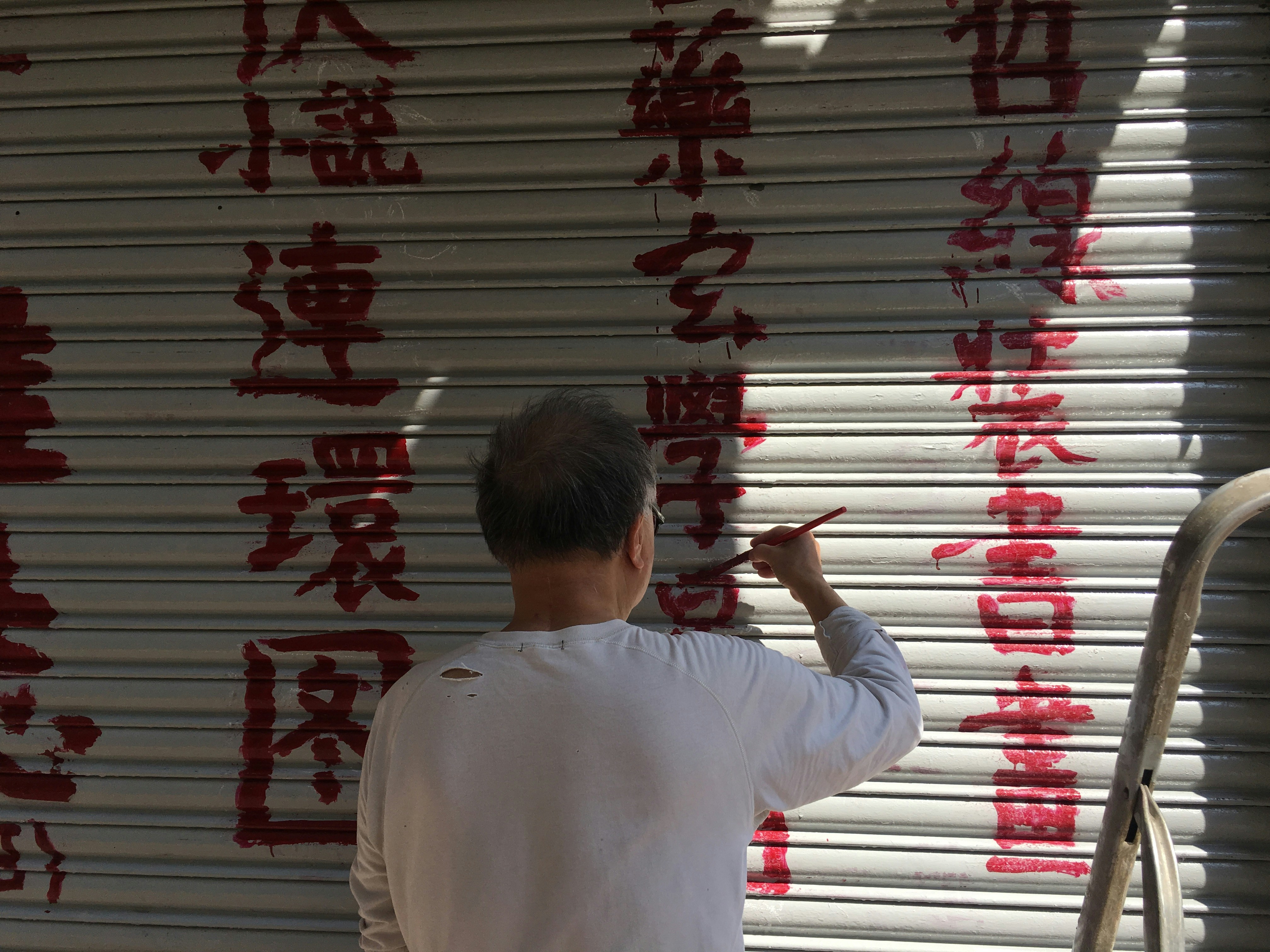 Chinese man painting red Chinese characters on shop front