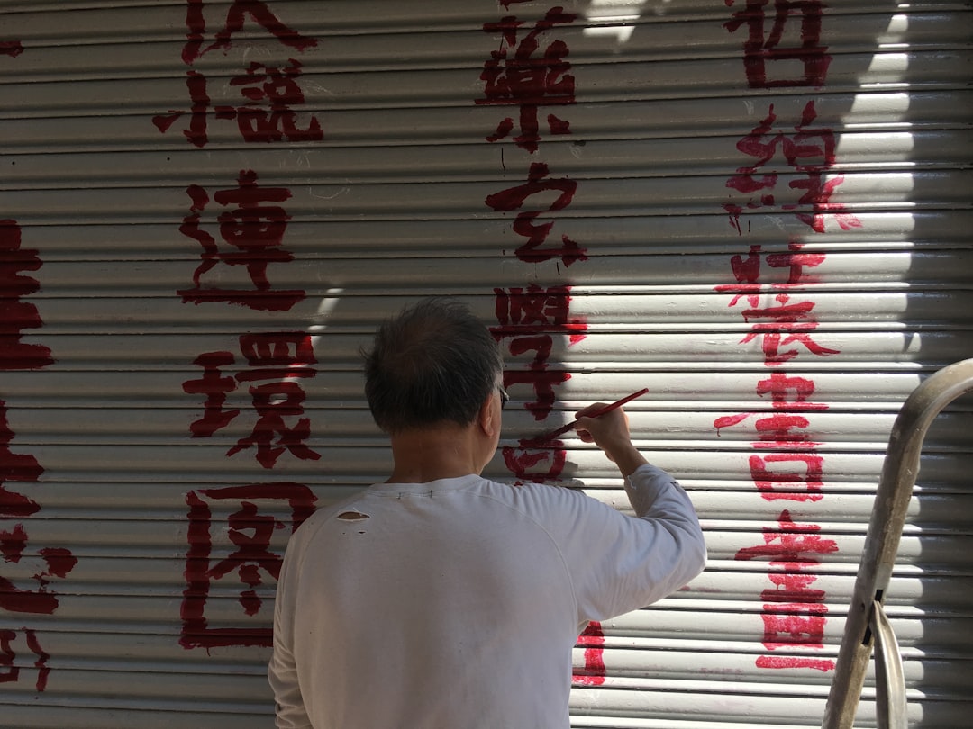 man painting Kanji text on roll-up door, Chinese man painting red Chinese characters on shop front