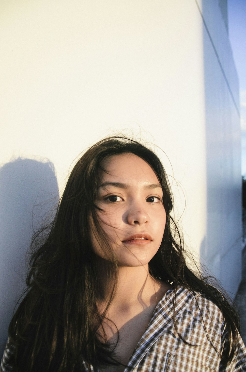 woman wearing blue and brown plaid dress shirt near white wall