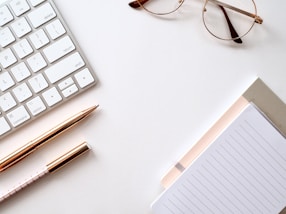 caneta próxima a bloco de notas, teclado e óculos