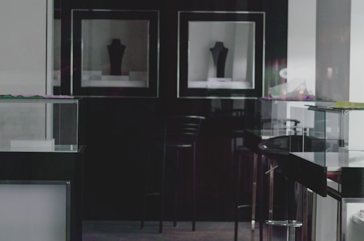 A dimly lit display room with dark walls and reflective glass cases. Two silhouette-shaped mannequin stands are visible in wall-mounted display boxes. The overall atmosphere is sleek and modern, with minimal decoration.