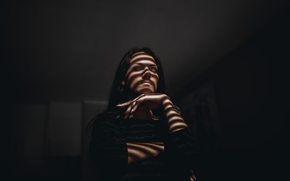 a woman standing in a dark room with her hands on her chest