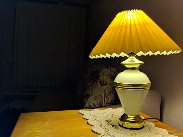 Close-up of a luxurious linen cushion next to a golden matte lamp on a light wooden side table.