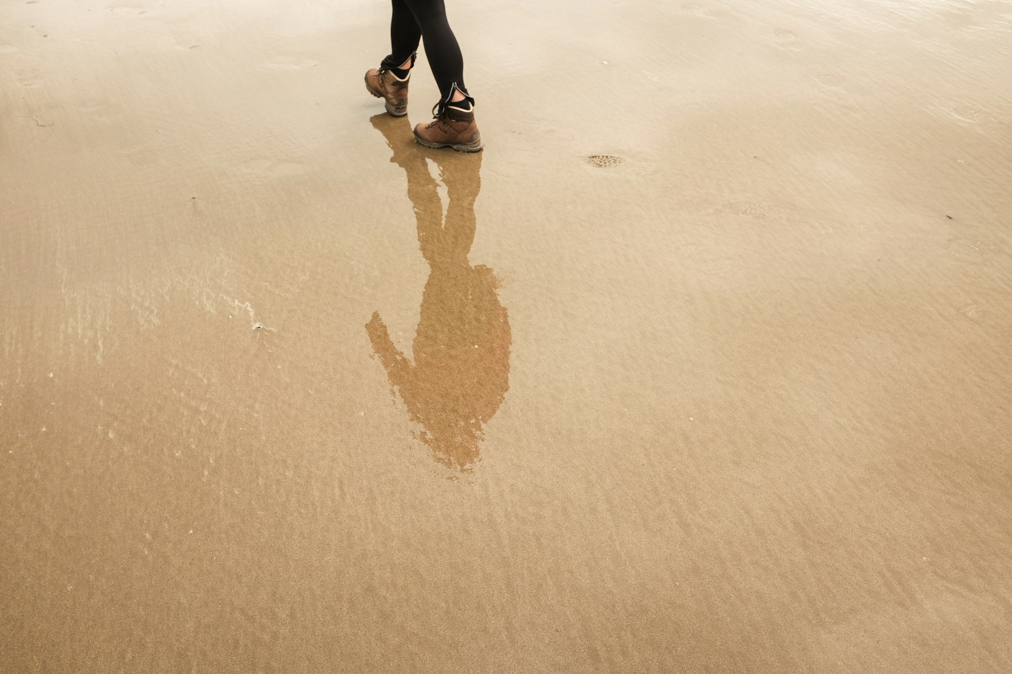 a reflection on the wet sand of a person walking along the beach