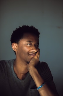 A person is resting their chin on their hand, appearing contemplative and relaxed. The lighting is soft, creating a calm atmosphere.