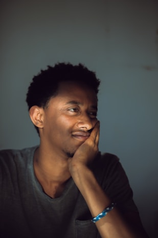 A person is resting their chin on their hand, appearing contemplative and relaxed. The lighting is soft, creating a calm atmosphere.