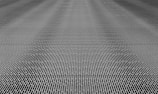 A close-up of a metal mesh structure with intricate interlocking patterns forming a grid-like appearance. The surface is composed of repetitive linear elements creating a sense of depth and complexity.