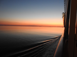 A serene cruise ship gliding through calm blue waters with a sunset sky.