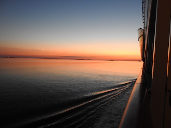 A serene cruise ship gliding through calm blue waters with a sunset sky.