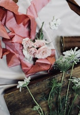 A delicate arrangement of soft pink and cream artificial flowers resting on a sage green velvet cloth.