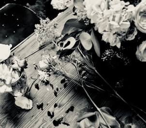 A black and white photograph of a simple arrangement of everyday objects on a wooden table, softly lit to highlight textures.