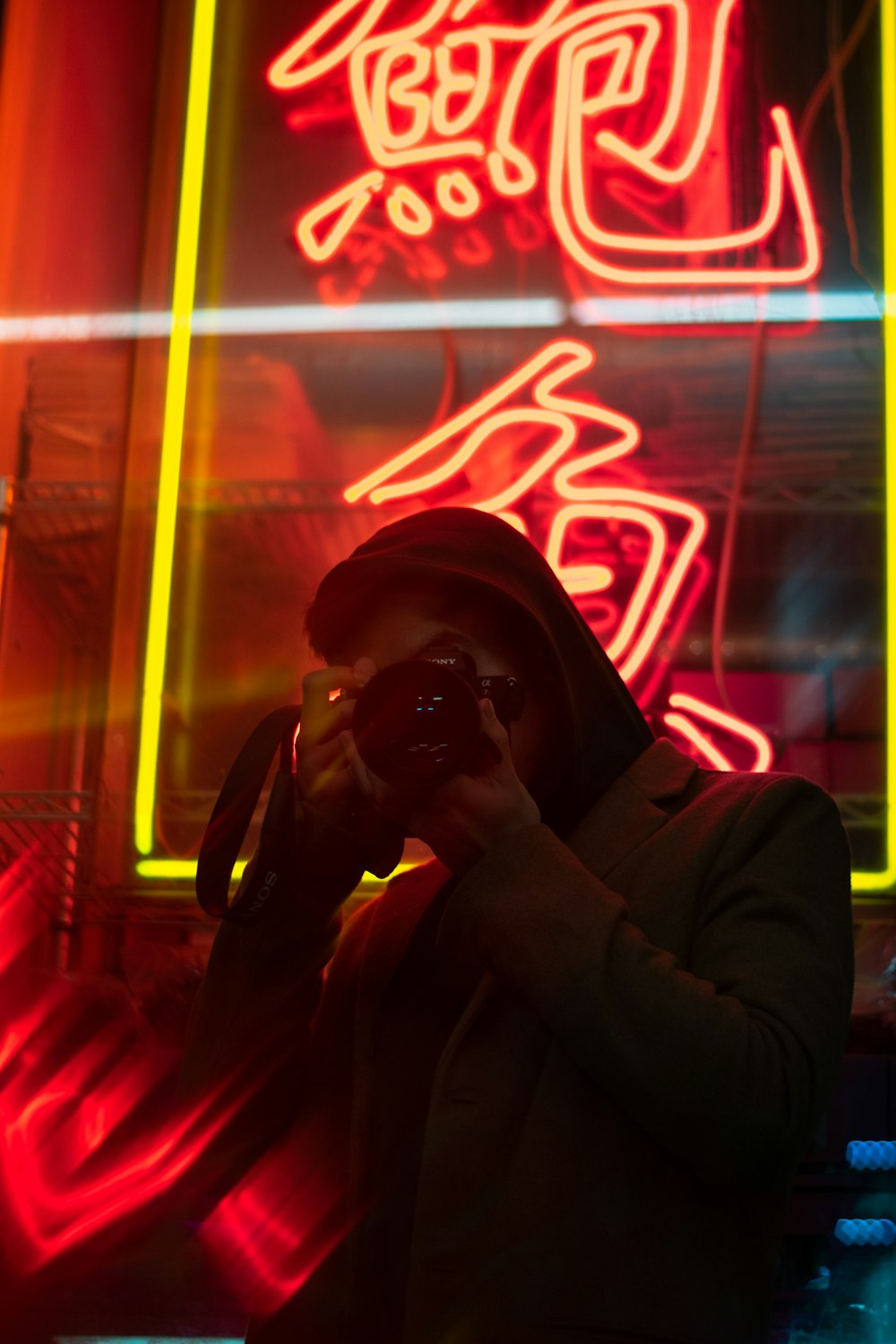 person holding DSLR camera near red neon signage
