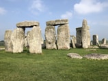 Ancient stone structures consisting of large upright stones capped with horizontal lintels located on a grassy landscape under a clear blue sky.