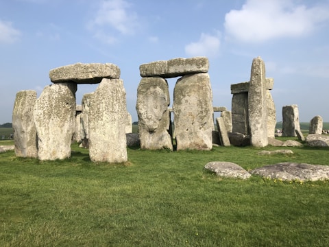 Ancient stone structures consisting of large upright stones capped with horizontal lintels located on a grassy landscape under a clear blue sky.