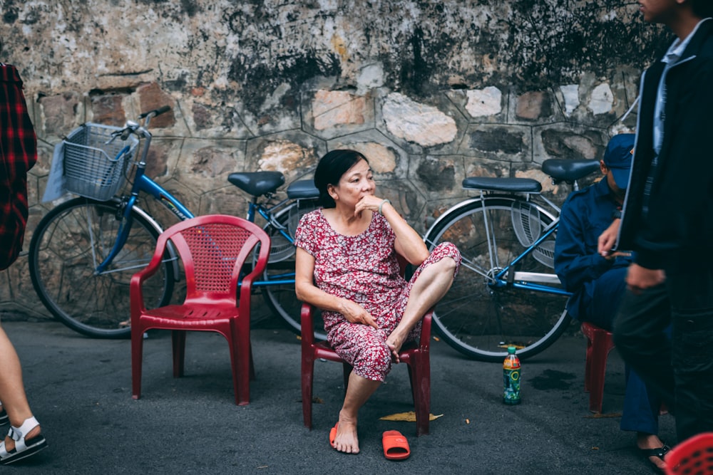 women in purple and white floral dress sitting on red plastic armchair outdoors