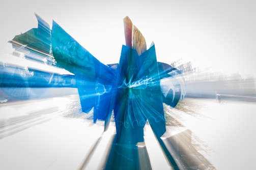 A modern abstract sculpture composed of blue geometric shapes with dynamic lines projecting outwards, creating a sense of motion against a light background.
