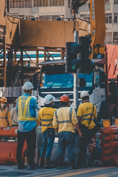 A group of diverse construction workers from various continents wearing helmets and high-visibility vests, collaborating on a site with clear safety protocols.