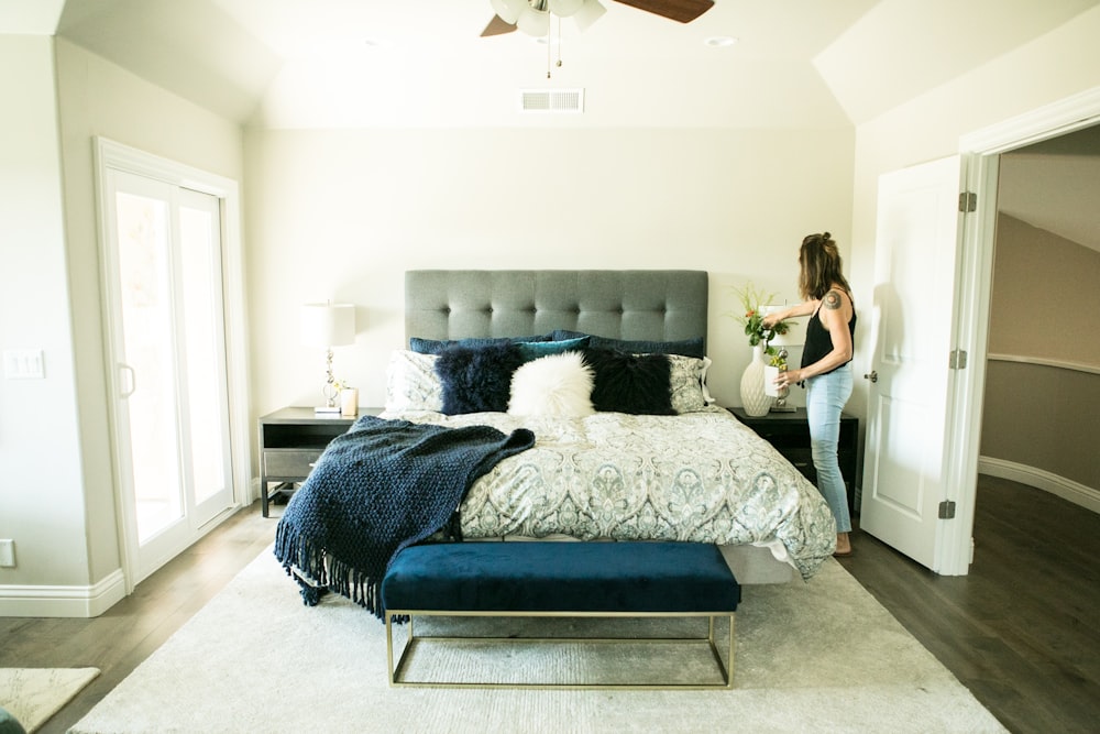 woman putting flower in vase beside bed