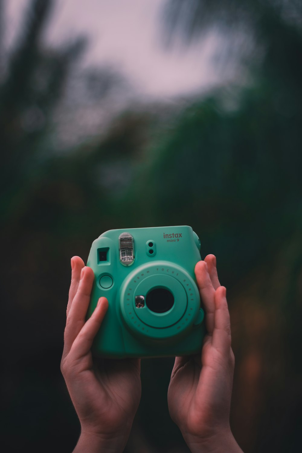 selective focus photo of person holding teal Fujifilm Instax instant camera
