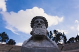 A close-up of a weathered stone statue of Zeus against a bright blue sky.