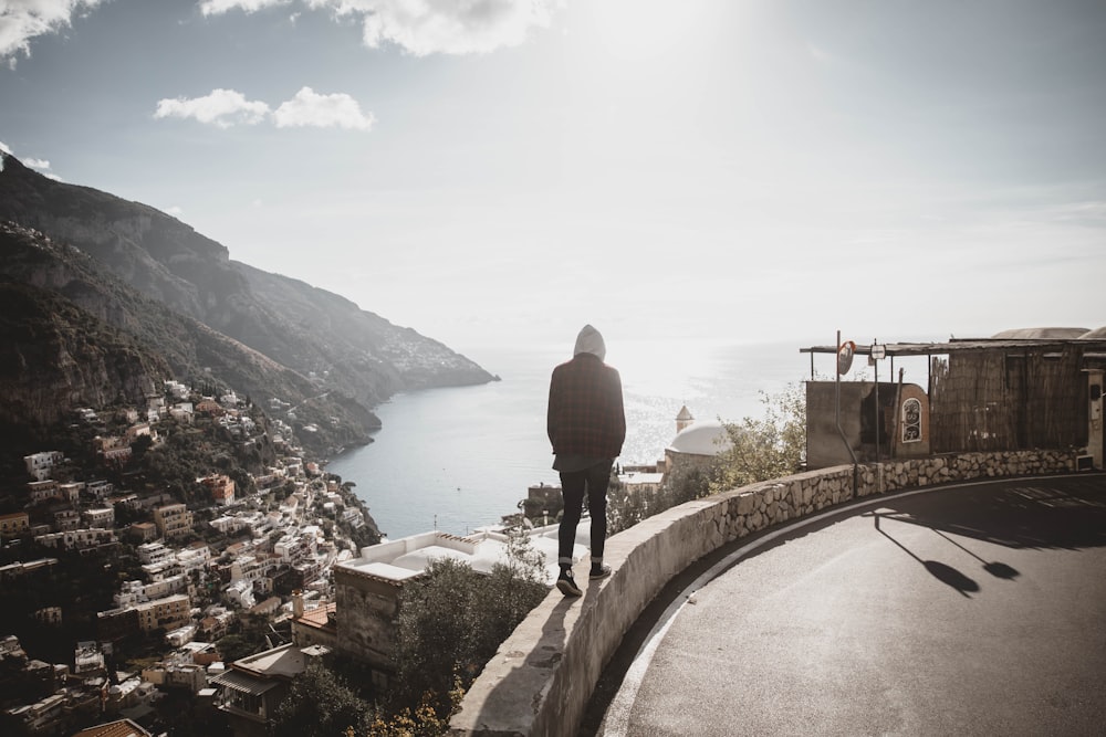 person standing on grey pavement overlooking body of water