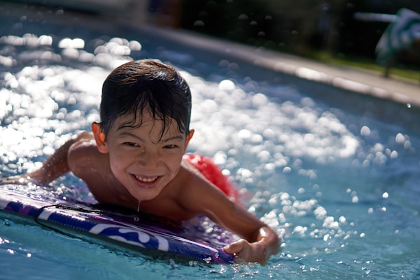 A joyful child learning to swim with an instructor in a bright pool.