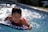 A happy child playing with colorful water toys in a backyard pool on a sunny day.