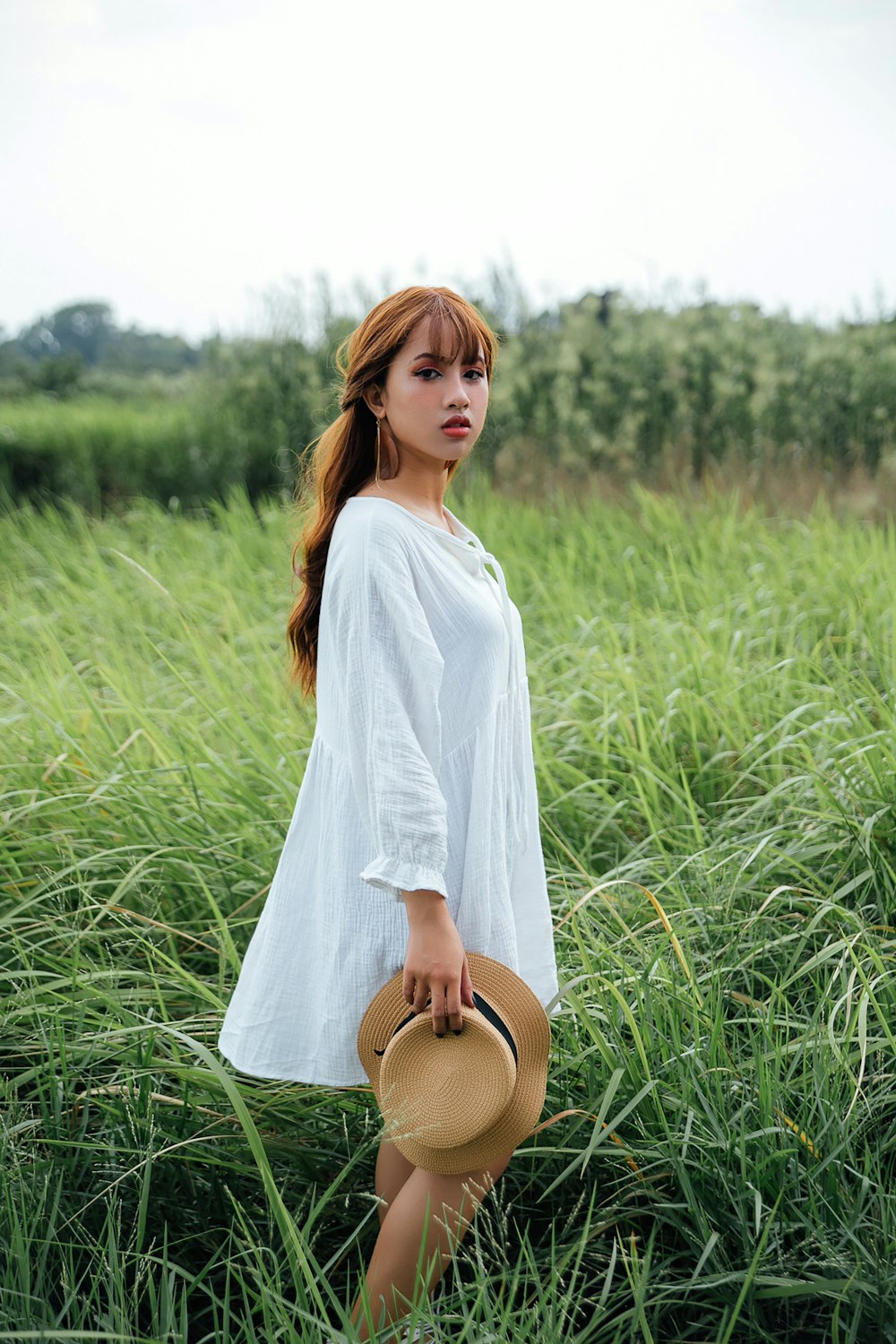 woman in white long sleeved dress holds brown hat