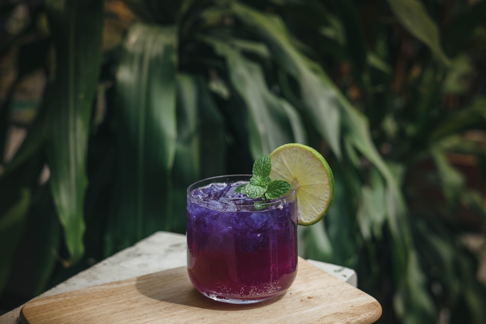A glass filled with purple and blue liquid representing a floral milk tea beverage with boba pearls