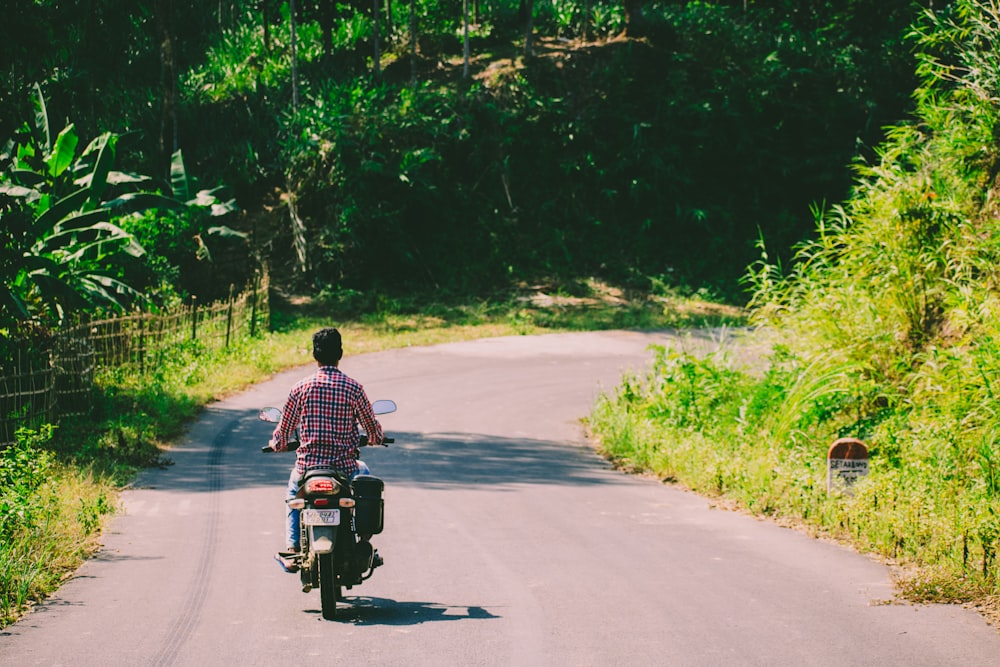 man riding motorcycle on road between trees