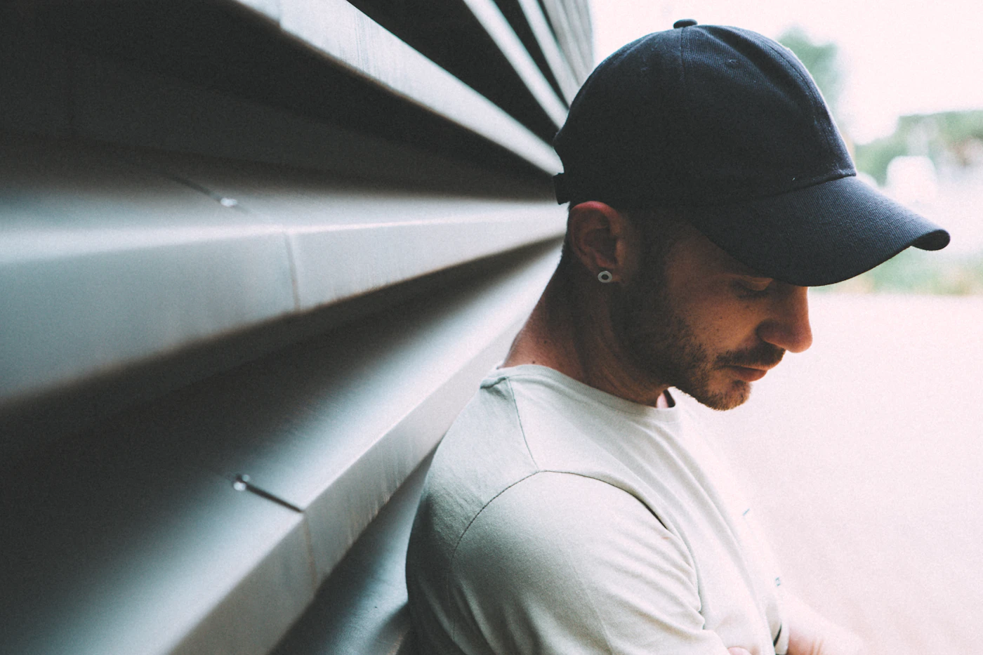 Man wearing a black cap and white shirt leaning on a gray metal wall