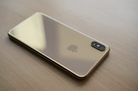 A luxury smartphone with a glossy navy back and delicate gold edges, displayed on a dark wooden table.