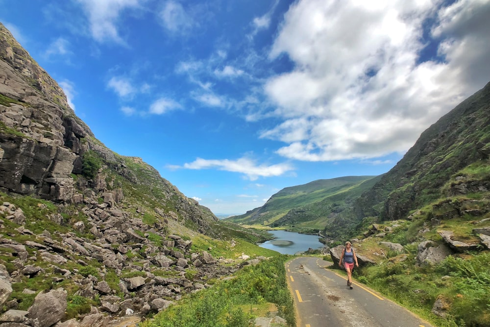 woman walking on road between mountains