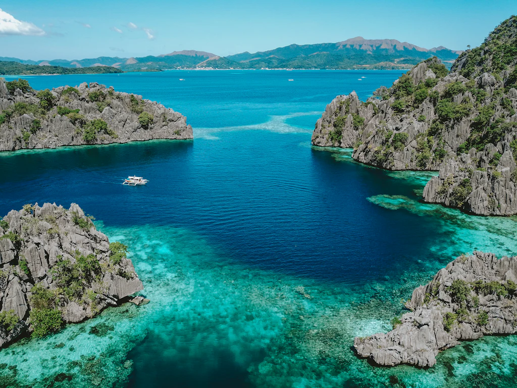 A banca crossing turquoise water between jagged limestone islets in Coron, Palawan