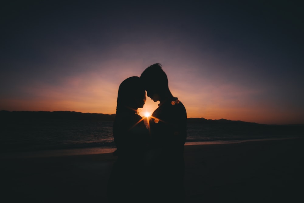 Mann und Frau stehen während des Sonnenuntergangs in der Nähe des Ufers