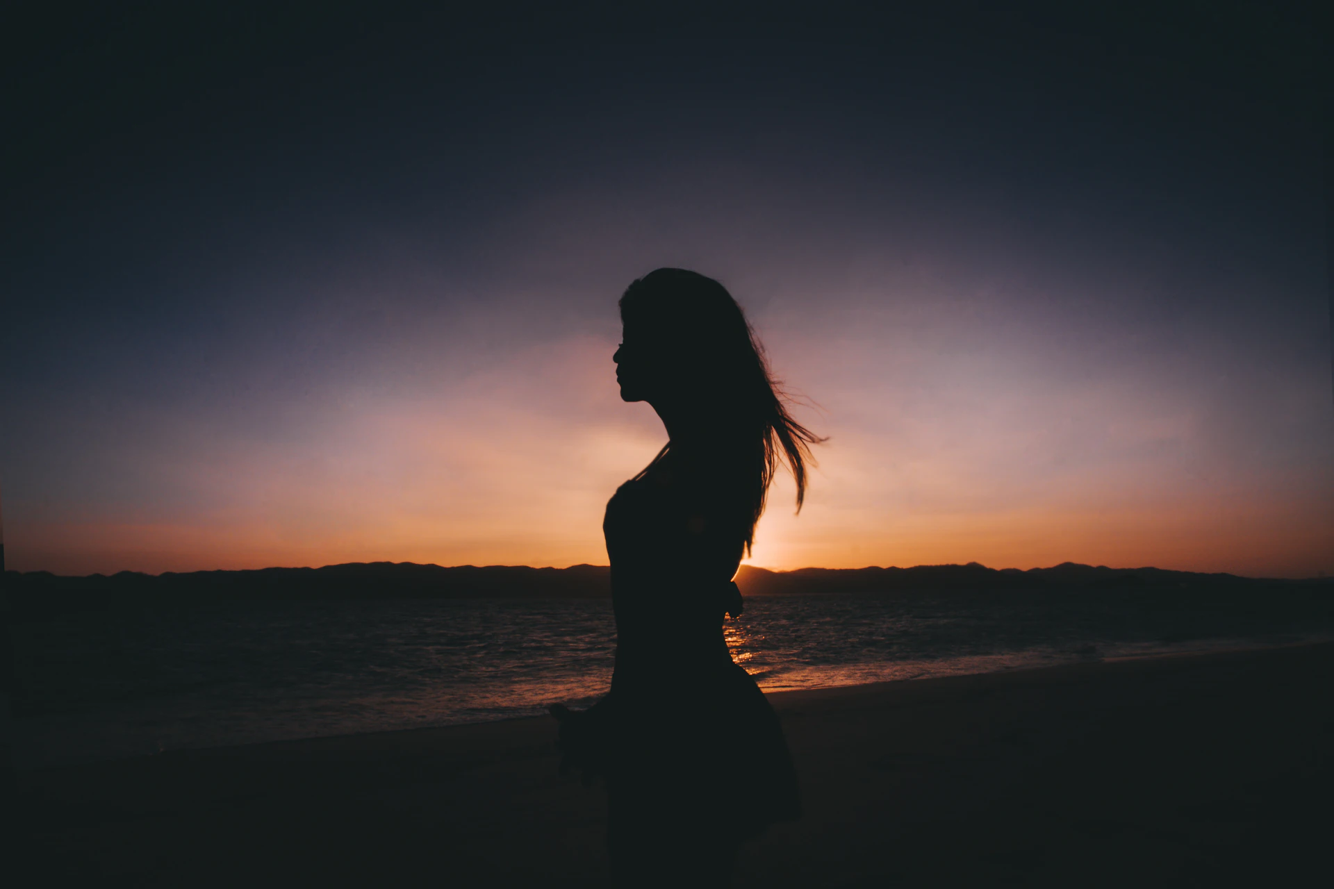 A silhouette of a woman standing peacefully near the seashore at golden hour