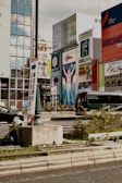 A bustling city scene with a large billboard featuring a triumphant athlete figure. Surrounding buildings showcase various advertisements, including ones for Asahi and other brands, against a backdrop of glass-clad structures.